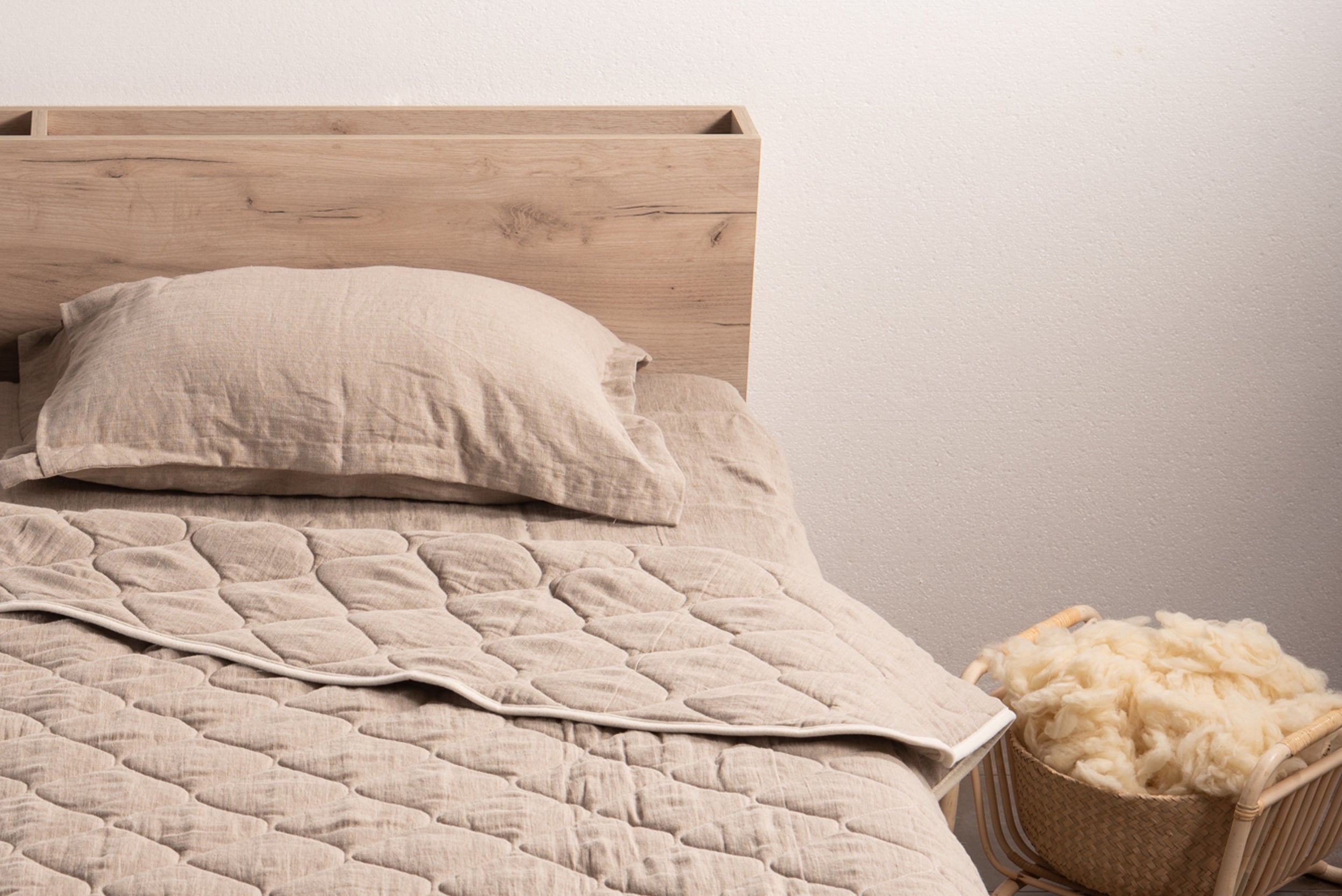 Natural linen pillowcase on bed with wooden headboard and woven basket with wool.