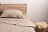 Linen pillow cover and quilt on bed with wooden headboard, showcasing natural hypoallergenic bedding in minimalistic bedroom setup.