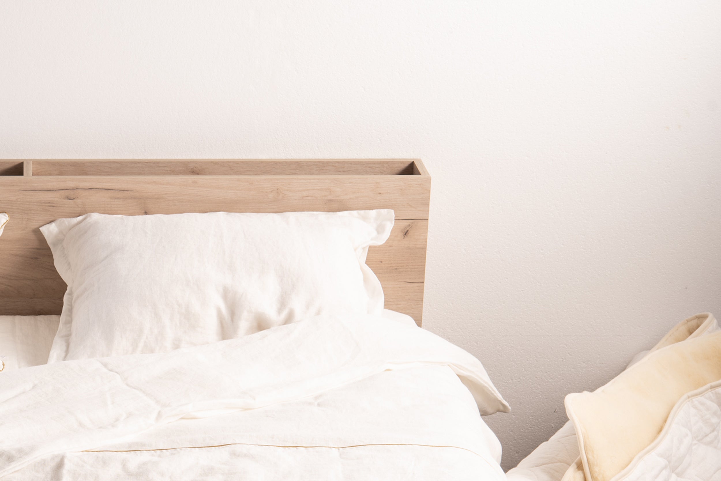 White Oxford linen pillowcase on a neatly made wooden bed in a minimalistic bedroom setting.